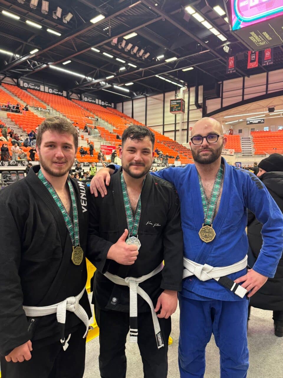 Trois jujiteiro médaillés posent dans un gymnase