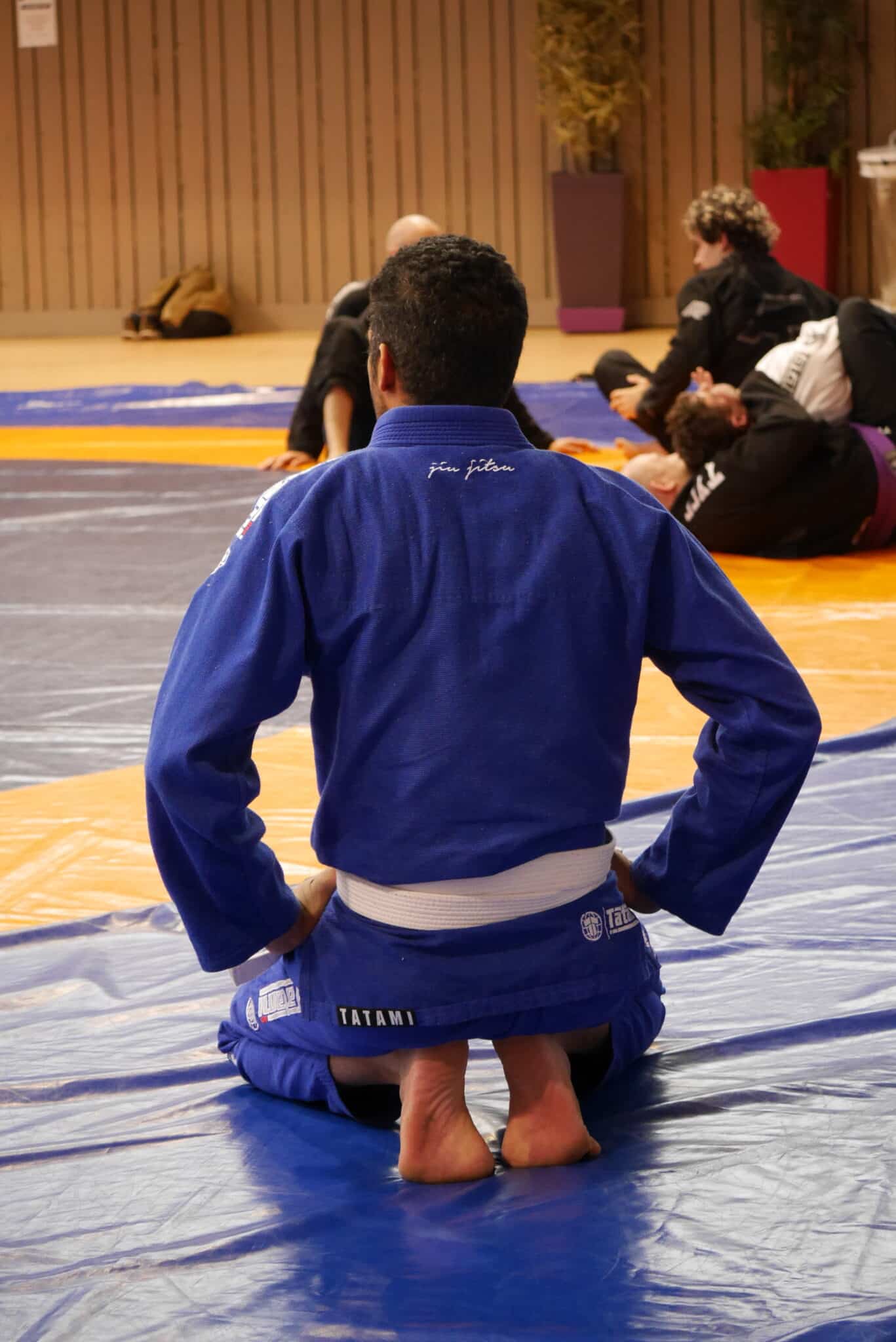 Pratiquant de jiu-jitsu en kimono bleu agenouillé sur tatami